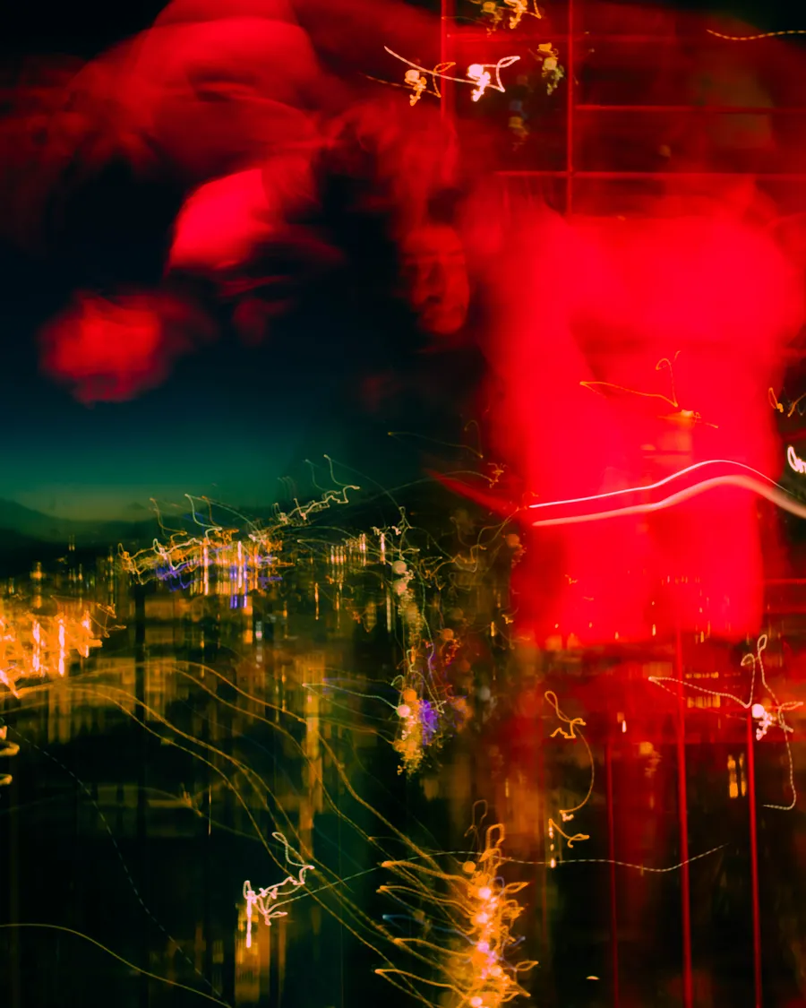 Fotografía de larga exposición en tonos rojos y dorados, con el movimiento de una mano y el perfil de JoshI4X entre luces urbanas nocturnas.